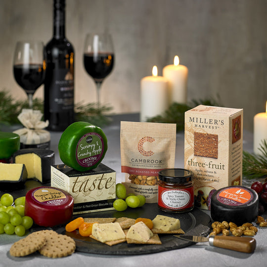 Cheese gift laid out on a table featuring wine & candles alongside artisan snacks and treats.